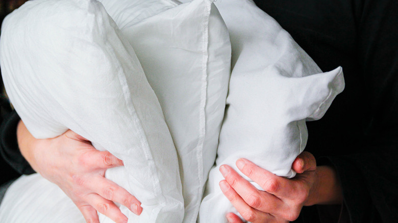 A pair of hands holds three white pillows.