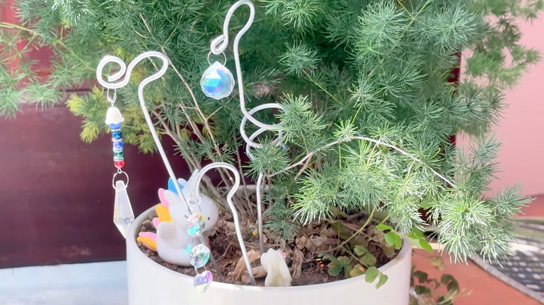 Beads and crystals hang from pieces of a hanger that have been put in a planter.