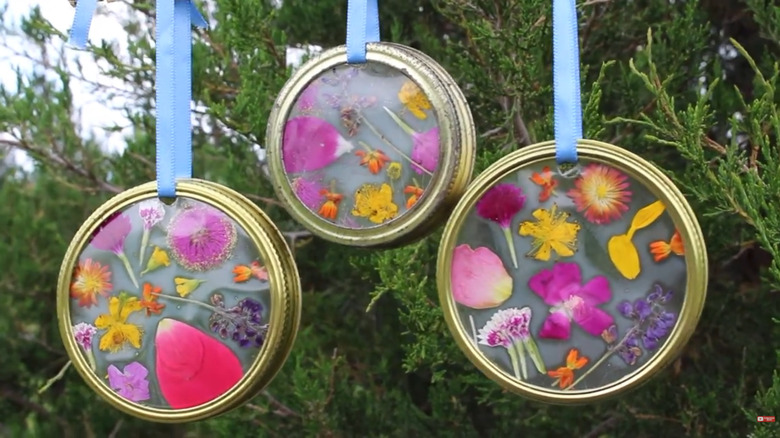 A windchime made of jar rings, ribbon, and flowers hangs.