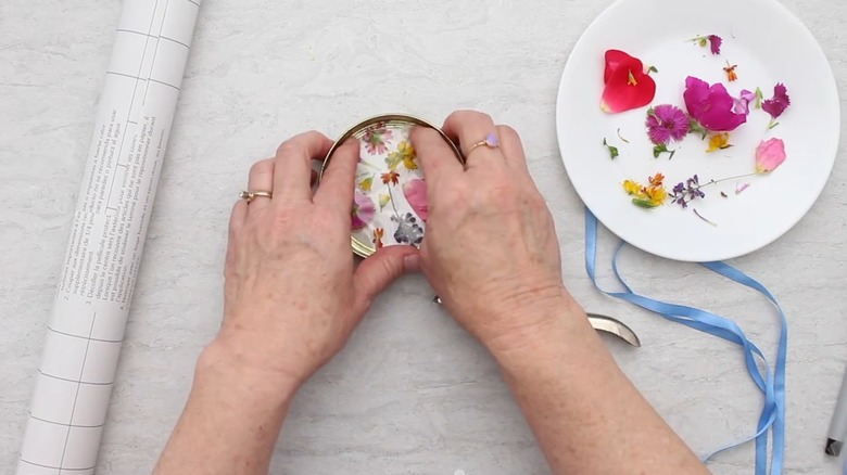 woman making jar lid garden décor diy with flowers and ribbon on table