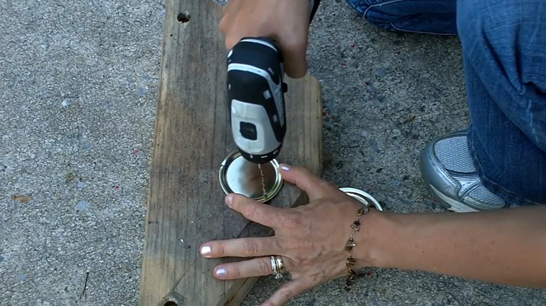 A woman drills into a mason jar lid.