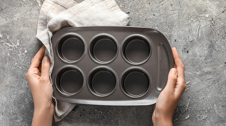 Hands hold a small muffin tin.