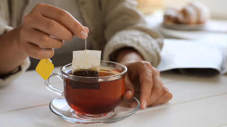 Woman lifts tea bag out of tea cup.