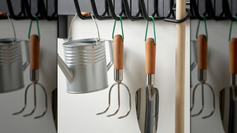 A LÄRKAR garden trowel and hand cultivator hang on hooks next to a watering can.