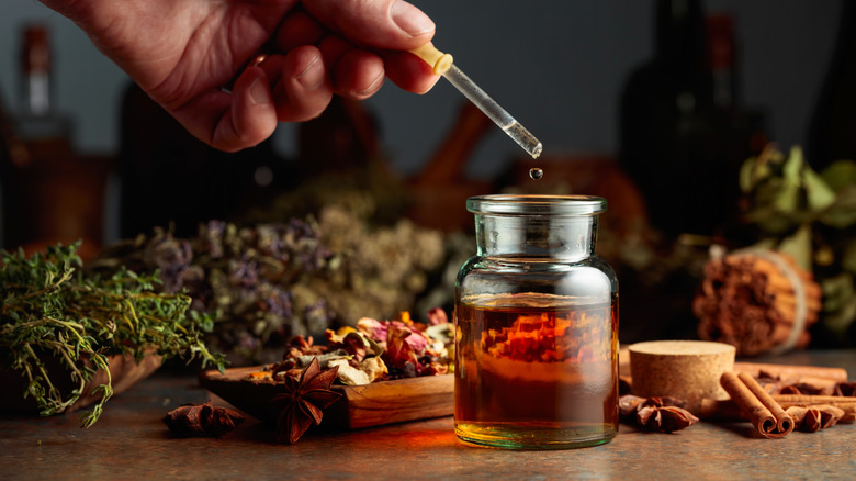 A hand is squeezing a dropper above a bottle of brown liquid.