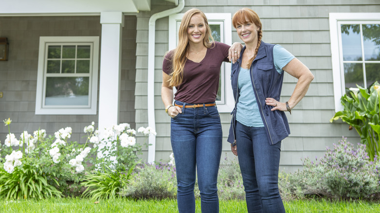 HGTV hosts Mina Starsiak and Karen E Laine stand in front of a house.