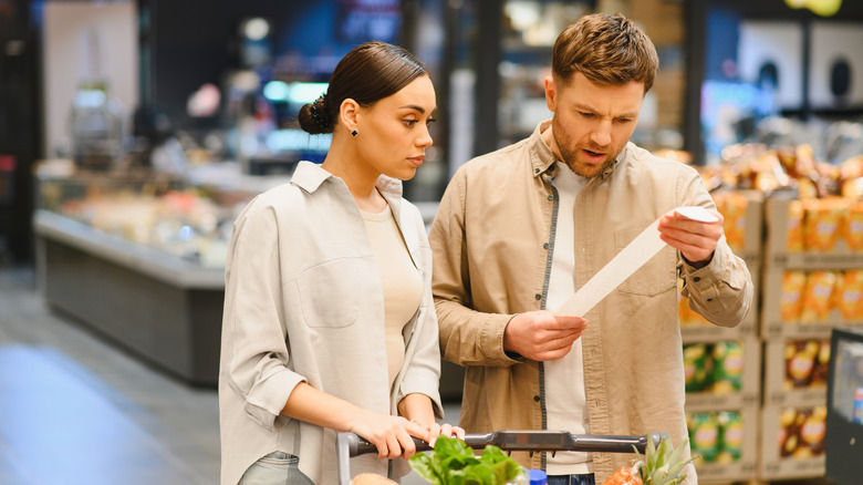 A couple looking at their receipt in frustration at a grocery store