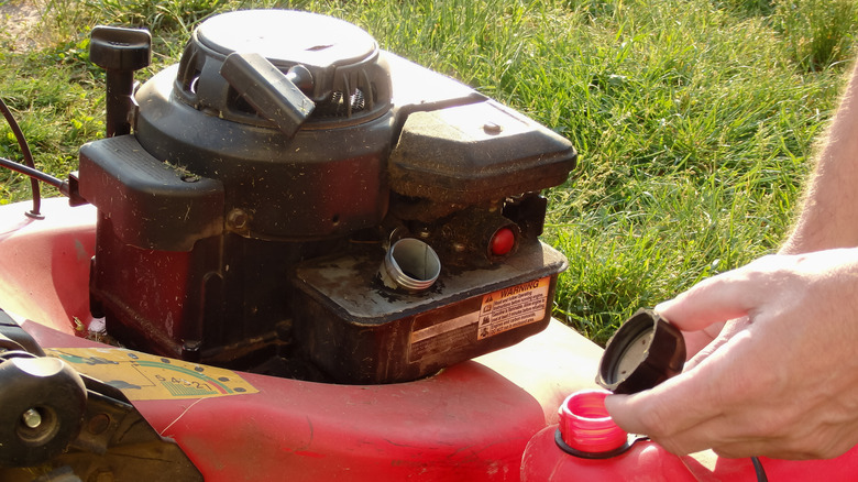 A person refills their lawn mower's gas tank.