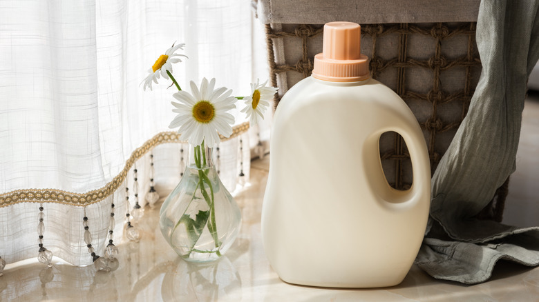 Laundry detergent bottle sits near a vase of daisies.