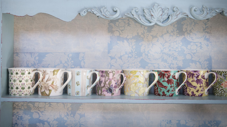 Floral mugs sit in a row on a light blue shelf.