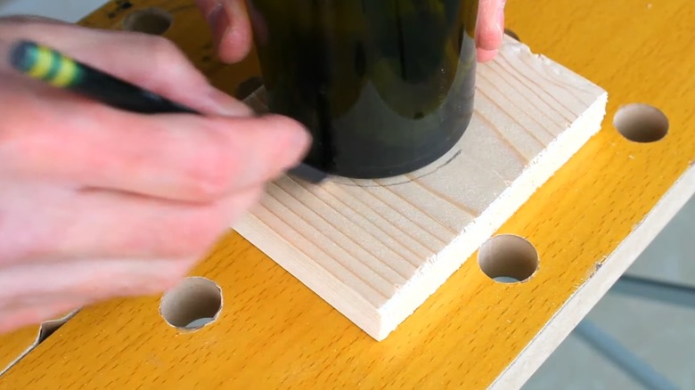 person tracing bottom of wine bottle on block of wood for DIY