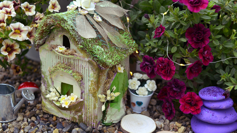 A miniature house is in a garden surrounded by flowers.