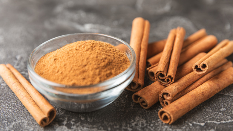 Cinnamon sticks and powder in a bowl sit on a counter.