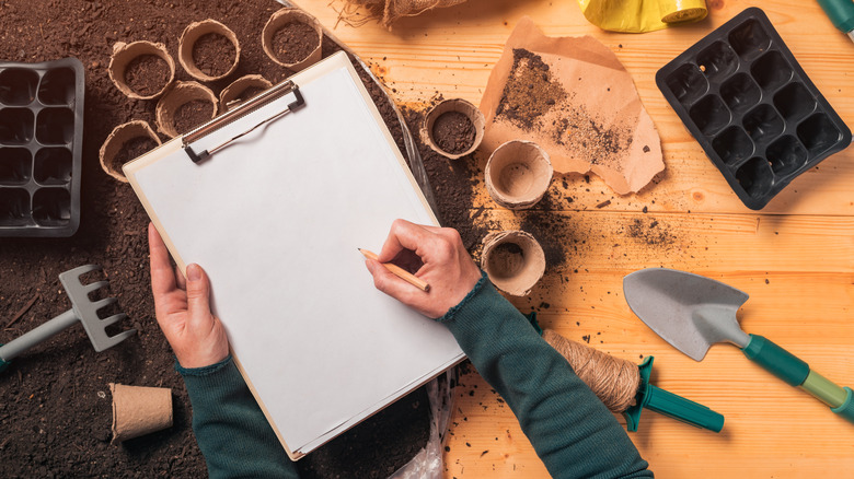 A person has paper and seed starting supplies to plan their garden.
