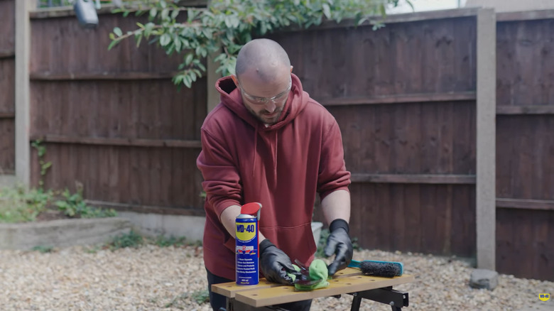A man polishes a lawn mower blade with WD-40.