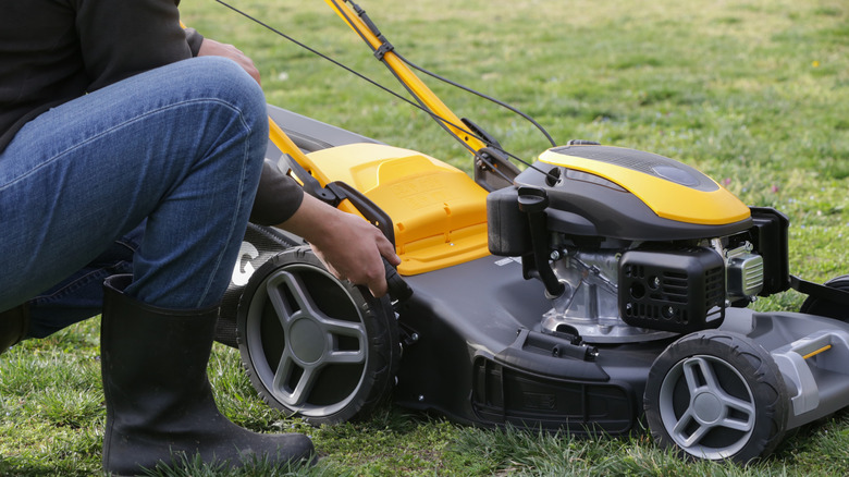 A person adjusts the height on their lawn mower.