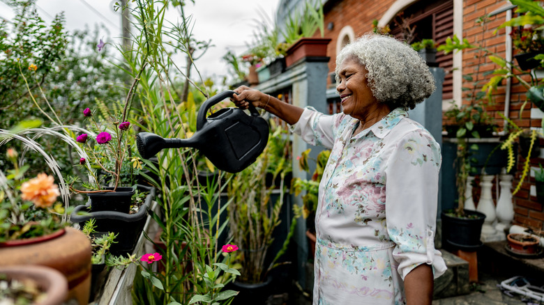 A woman uses a watering can to water a container garden.