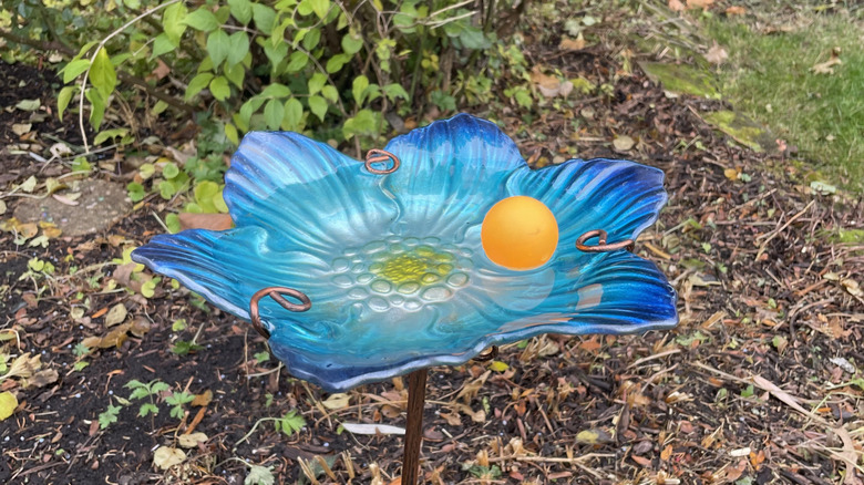 An orange ping pong ball floats in a blue, flower-shaped bird bath.
