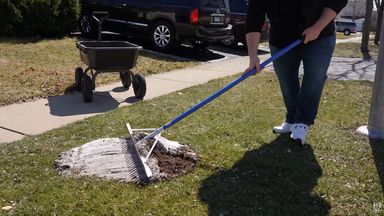 A landscaper uses a rake to smooth a mix of sand and potting mix into his lawn.