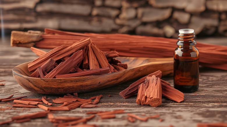A small uncapped brown bottle filled with liquid sits next to a small pile of red sandalwood sticks.
