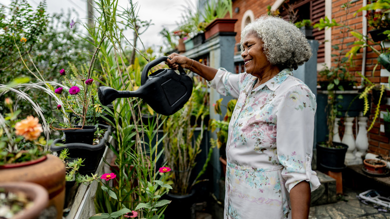 A smiling woman waters her plants with a watering can.