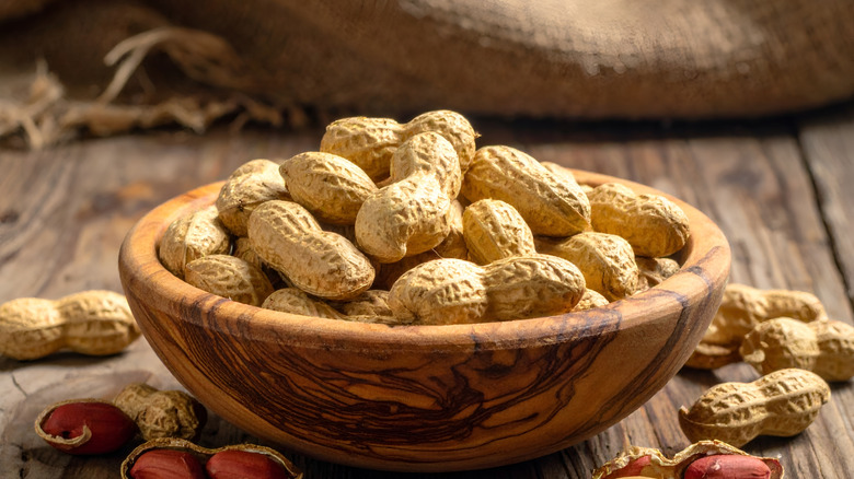 A wooden bowl is filled with peanuts in the shell.
