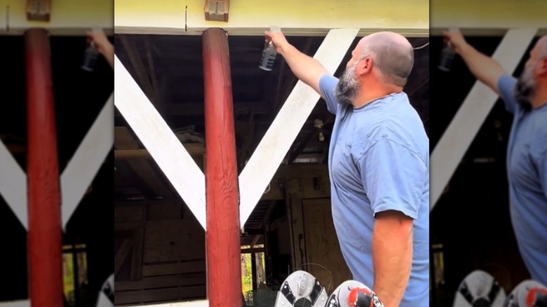 A man sprays almond oil and water mixture on wood barn.