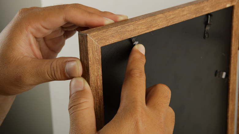 A man's hands holding a wooden picture frame with black backing.