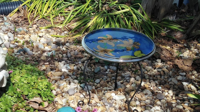 A birdbath made of a glass pot lid and a plant stand is painted and filled with water.