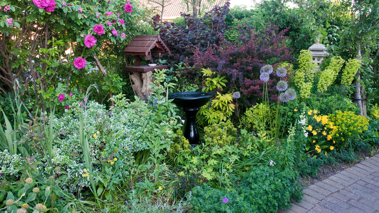 A lush garden has a birdbath, bird feeder, and other decor.