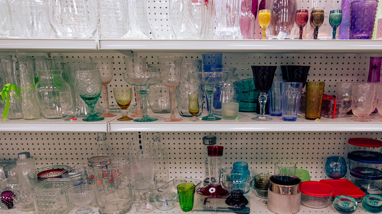 Thrift store shelves hold glass cups, bowls, and vases of various colors.