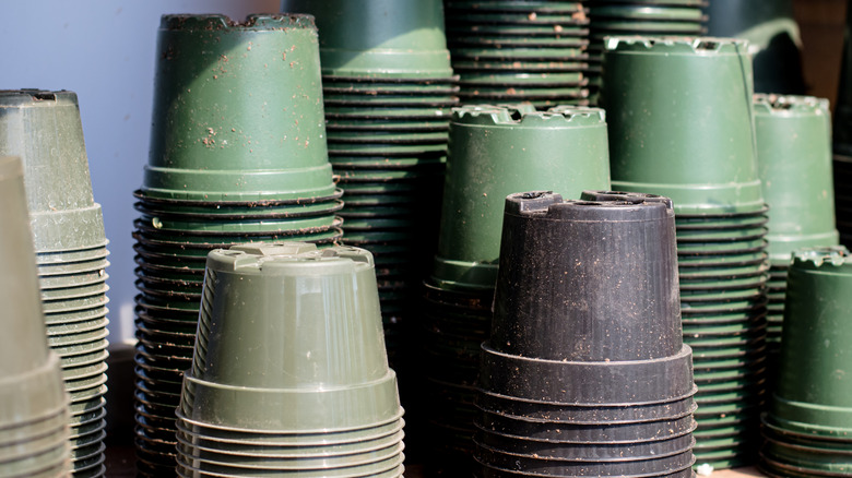Used green and black nursery pots are stacked upside down.