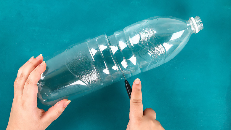 Hands cutting a clear plastic bottle in half on a turquoise background