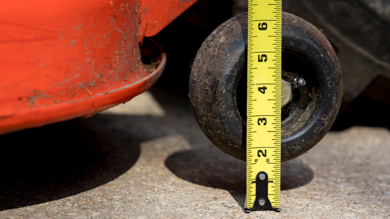 A tape measure is being used to check the height of the mower deck and blade.
