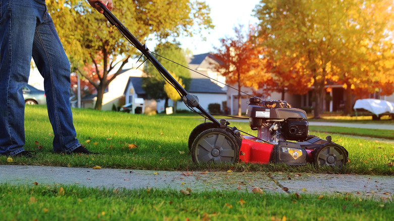 A gardener pushes their lawn mower on a fall day.