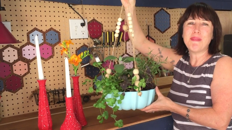 A woman holds a painted Bundt pan full of herbs and plants.