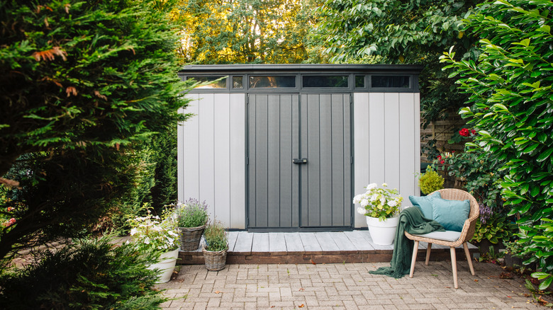A plastic shed is surrounded by trees in a garden.