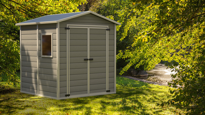 A plastic storage shed in in a lawn by a creek.