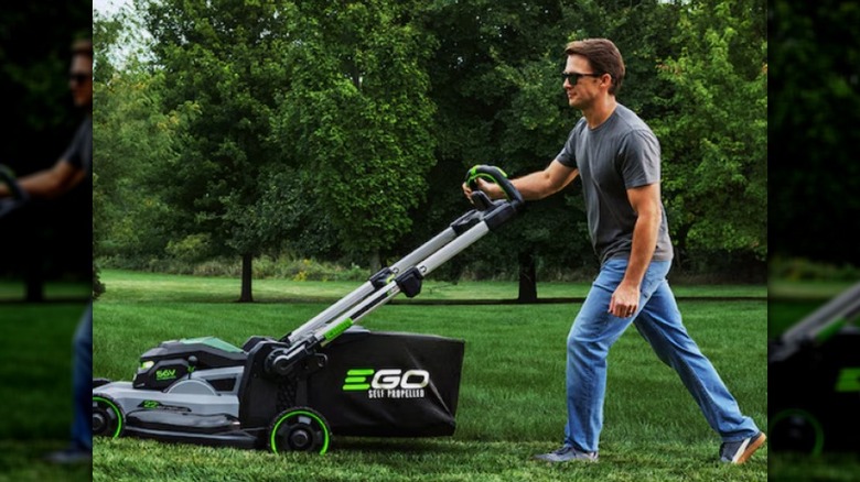 A gray and green Ego LM224SP-2 lawn mower being pushed by a man in a grey shirt.
