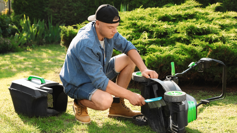 A young man cleaning a lawn mower with a brush