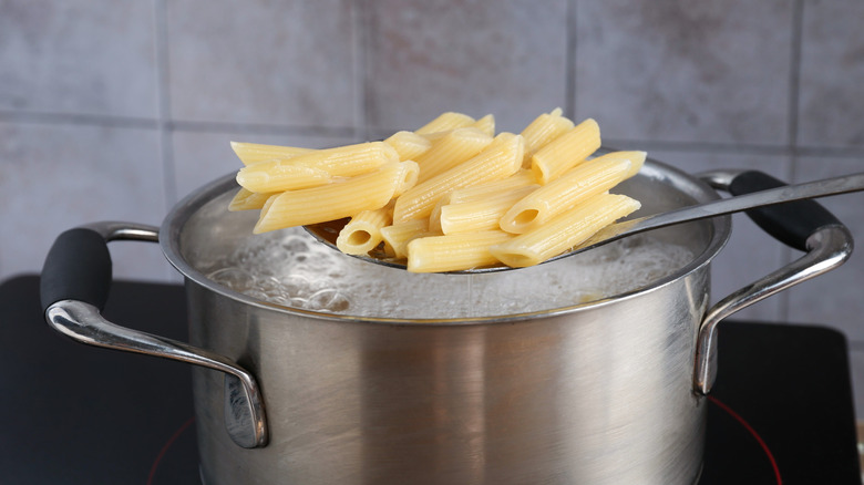 A pot of boiling water with a spoonful of penne pasta in front.