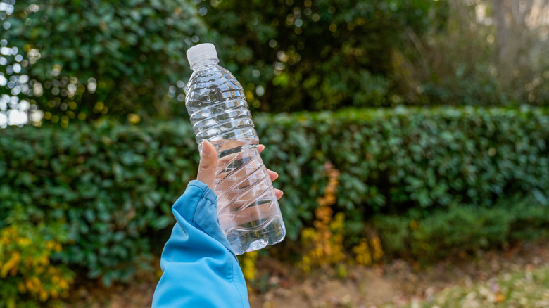Woman holding a plastic bottle outside in the yard.
