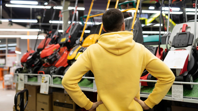 Man inspects lawn mowers at shop.
