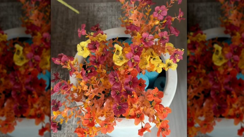A woman places faux flowers into the centers of pool noodles that are inside a planter.