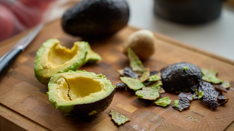 An avocado has been peels and the skins are on the cutting board.