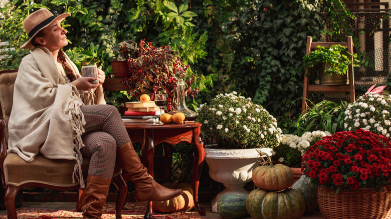 A woman sits outside in her autumn garden. Flowers and herbs grow in pots nearby.