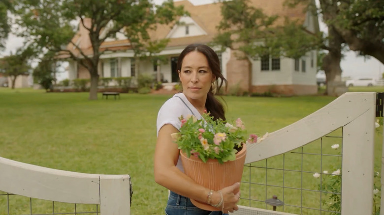 Joanna Gaines walks through a garden gate holding a basket of flowers.
