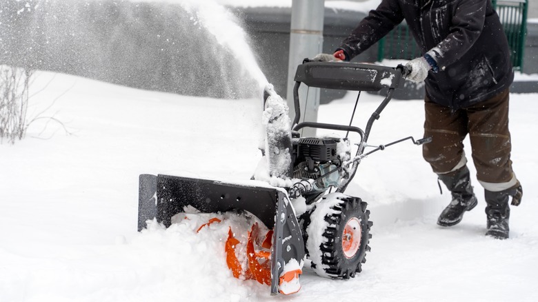 A homeowner pushes a snow blower.