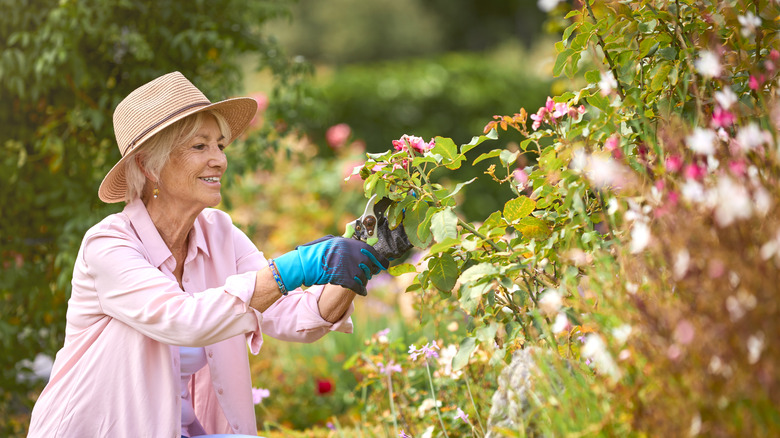A woman prunes in a garden with a hat and gloves on.