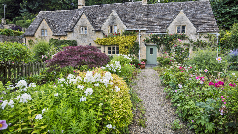 A thriving garden blooms on both sides of a gravel path by a cottage.